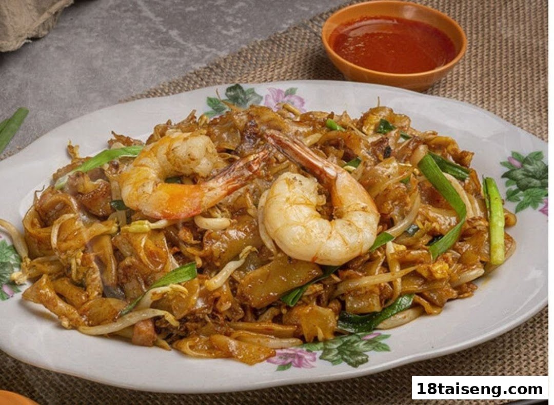 A close-up of a plate of stir-fried noodles with large prawns and vegetables, served with chili sauce.