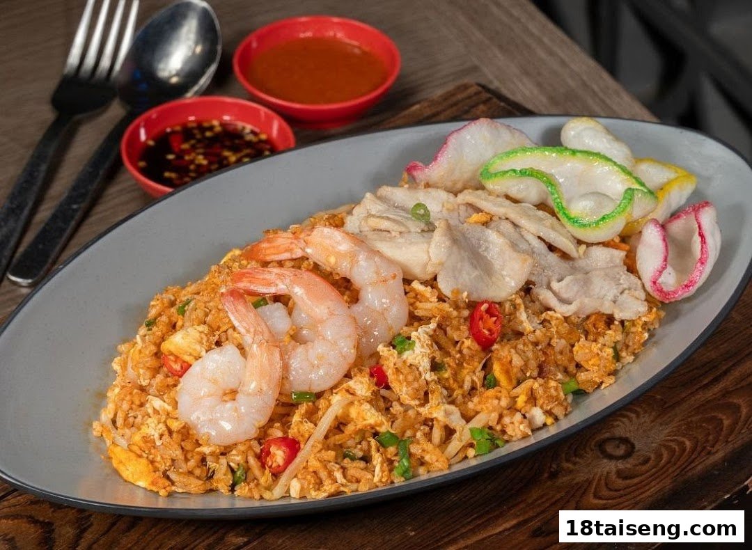 A vibrant plate of fried rice with shrimp, sliced pork, and colorful prawn crackers, served with sauces.