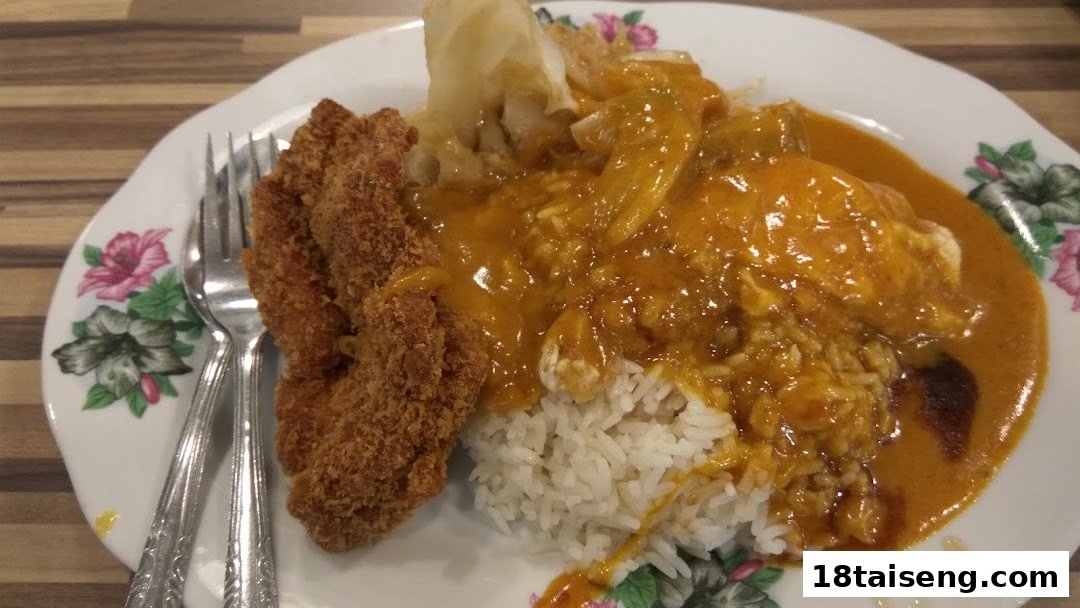 A plate of rice with crispy fried cutlet, rich curry sauce, and vegetables, served with cutlery.
