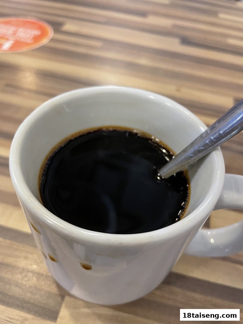 A white mug filled with black coffee and a spoon on a wooden table.