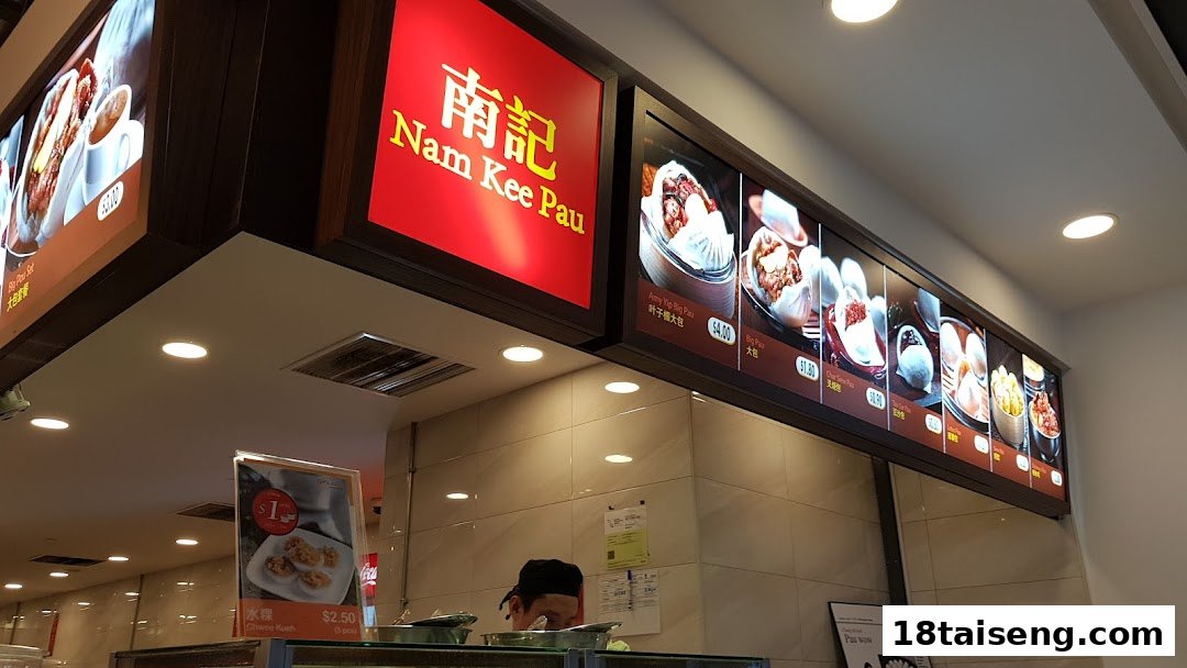An interior view of Nam Kee Pau, showcasing its illuminated menu boards and a staff member.