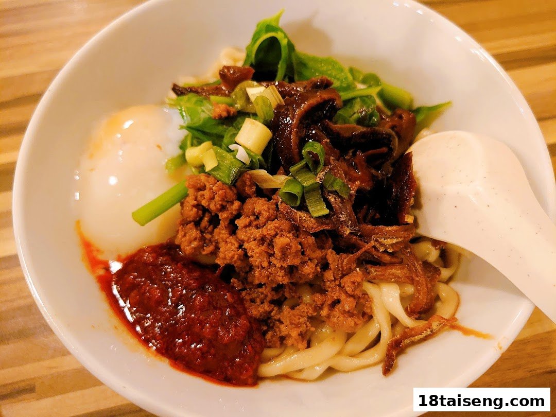 A close-up of a delicious bowl of noodles with minced meat, chili, egg, and greens.