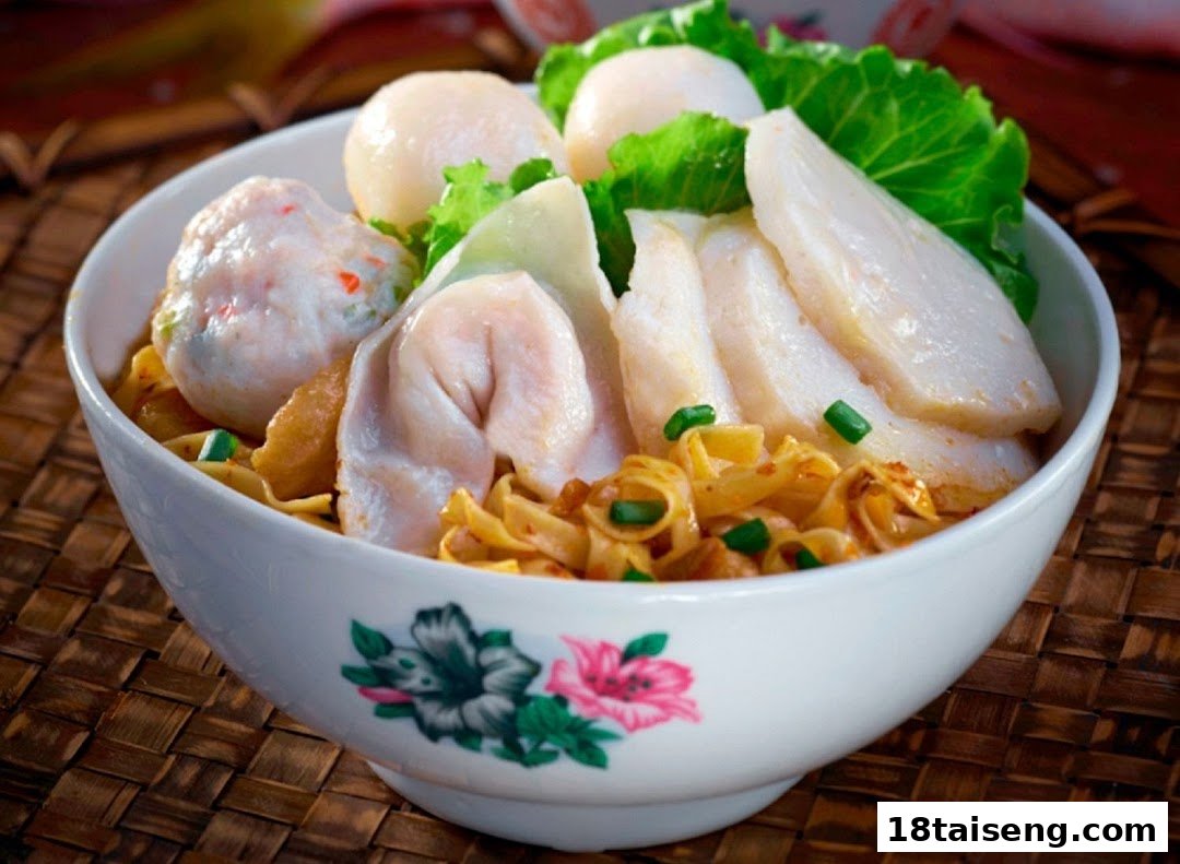 A vibrant bowl of noodles topped with fish cakes, dumplings, and fresh greens.