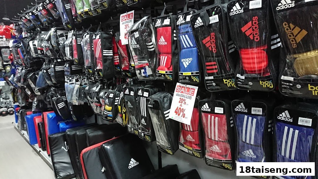 A retail display wall showcasing various Adidas boxing gloves and other combat sports equipment, some on sale.