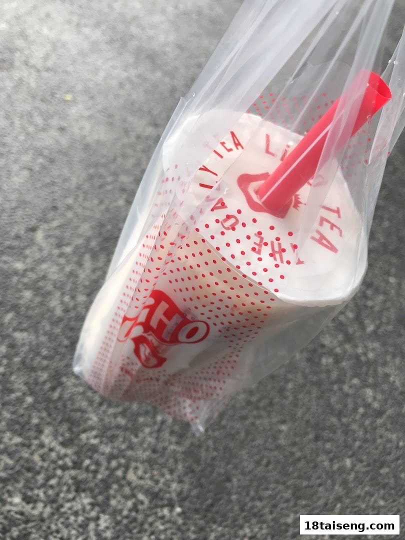 A LiHO TEA bubble tea cup with a red straw, in a clear plastic bag, resting on a grey surface.