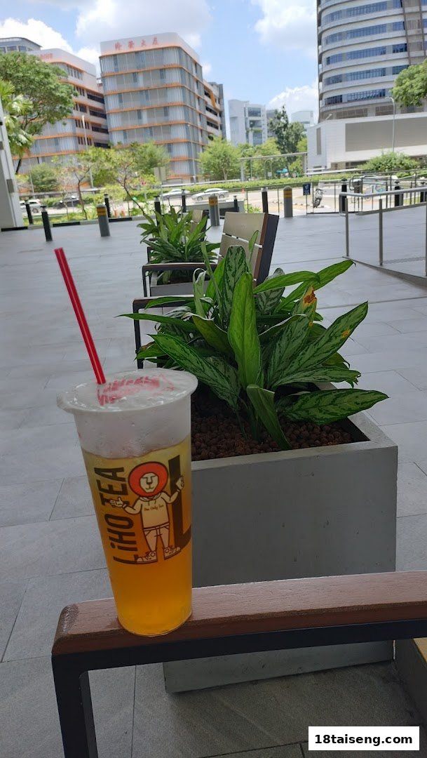 A LiHO TEA drink with a red straw on an outdoor bench, with buildings in the background.