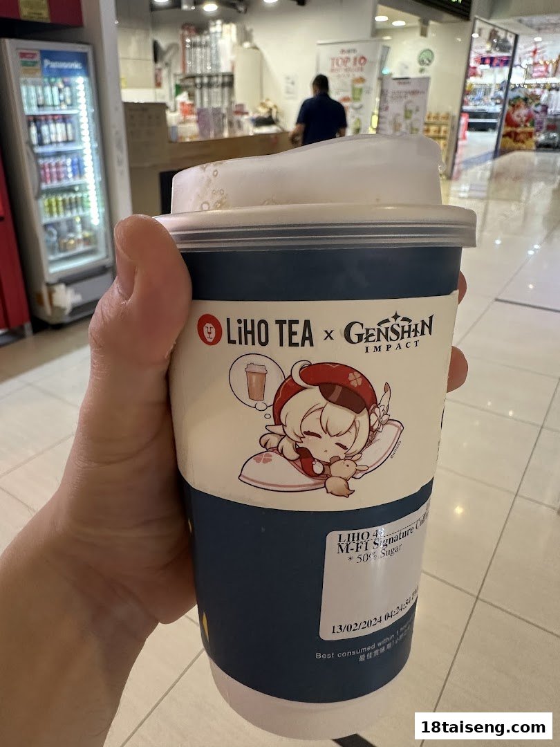 A hand holds a LiHO TEA x Genshin Impact collaboration drink cup inside a shopping mall.