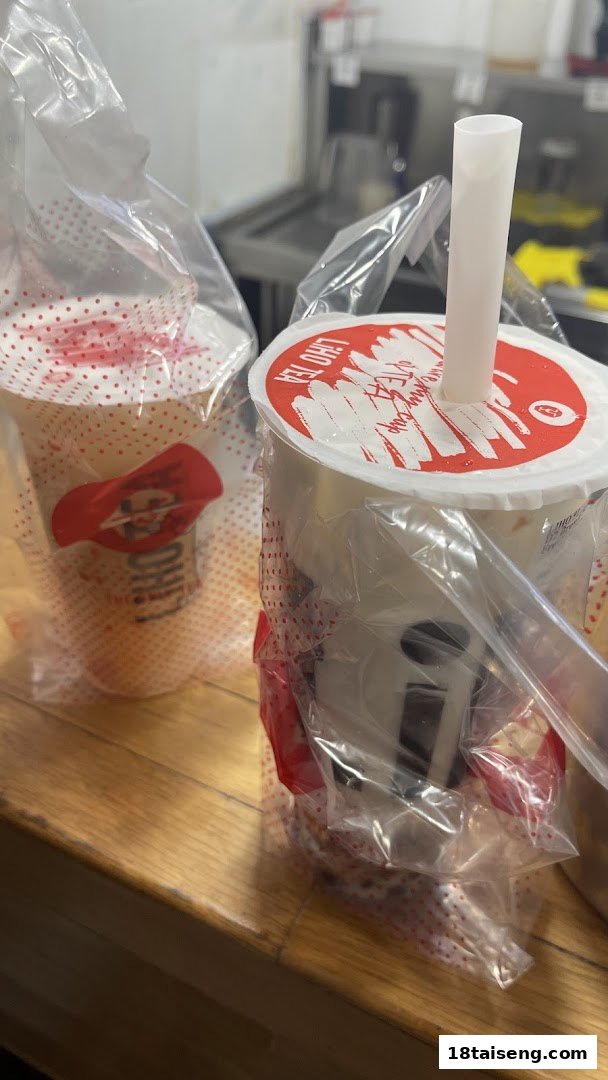 Two freshly prepared LiHO TEA bubble tea cups, one with a straw, on a wooden counter.