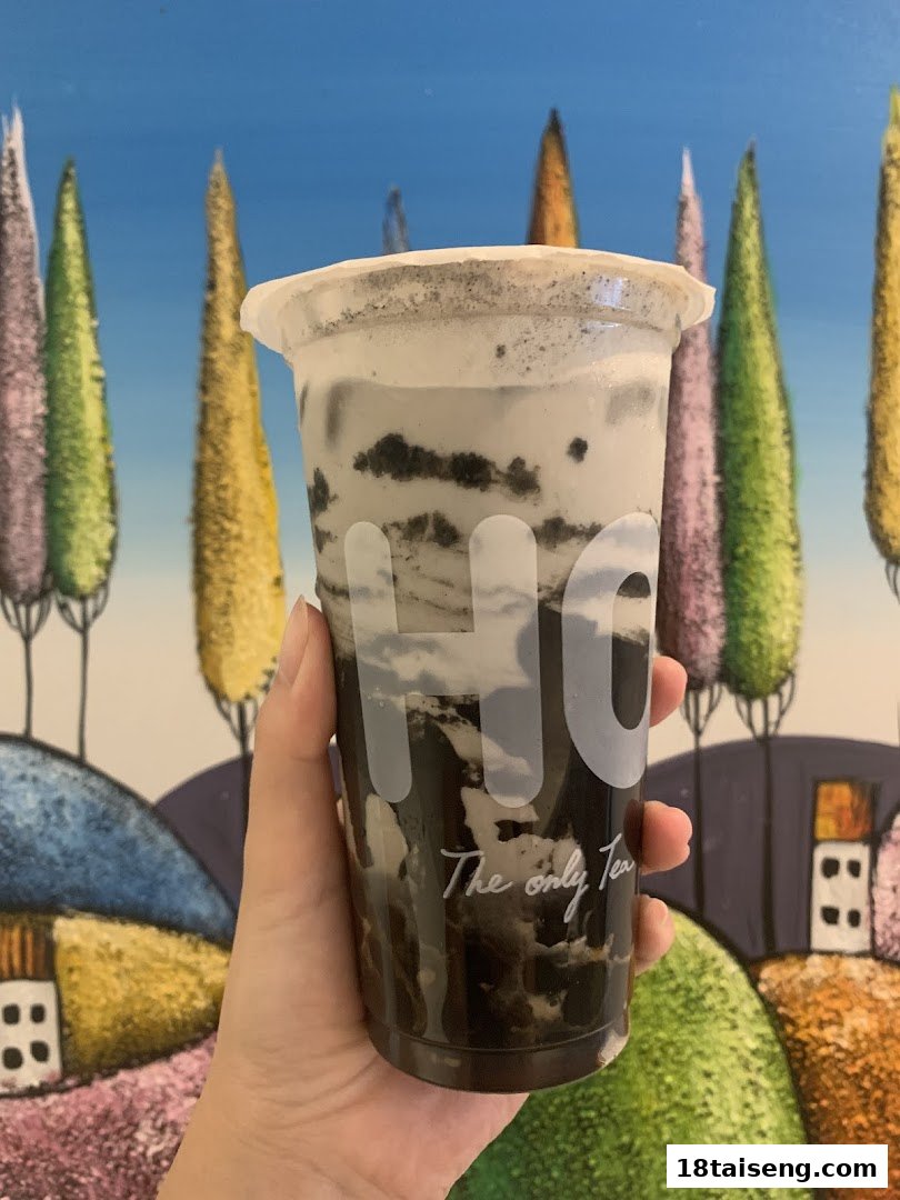 A hand holds a delicious-looking bubble tea with creamy layers and cookie bits.