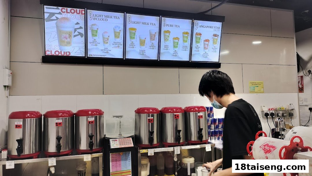A staff member prepares drinks behind a counter with digital menu boards displaying various bubble tea options.