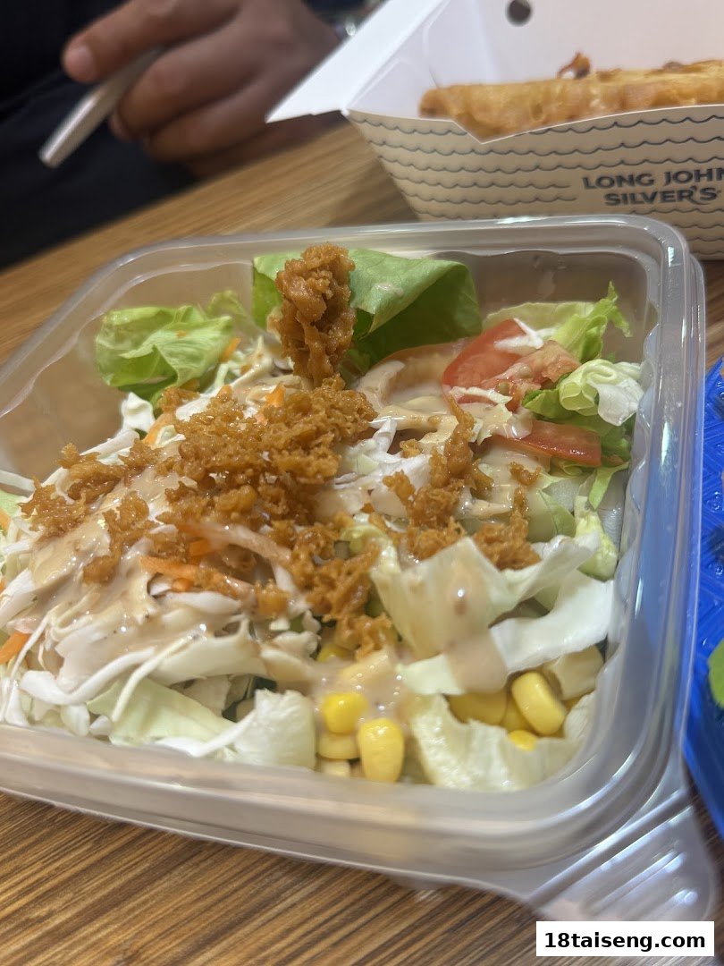 A fresh salad with dressing and crispy toppings, next to fried seafood from Long John Silver's.