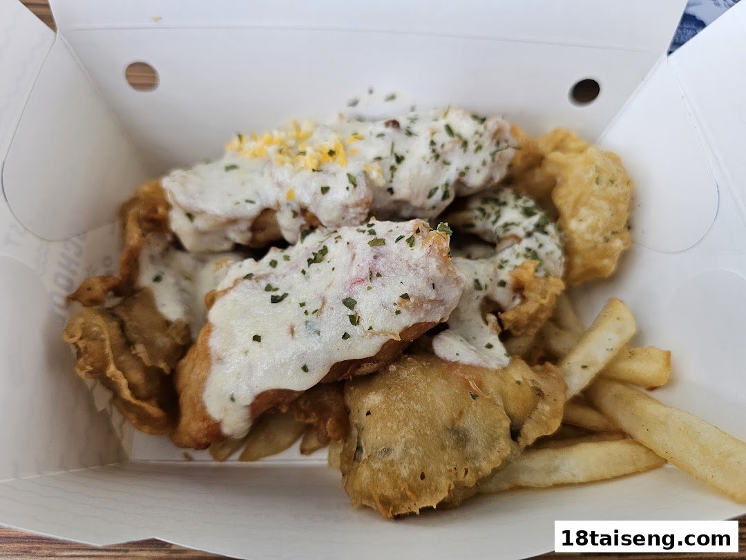 A box of crispy fried seafood and fries, topped with creamy sauce and herbs.