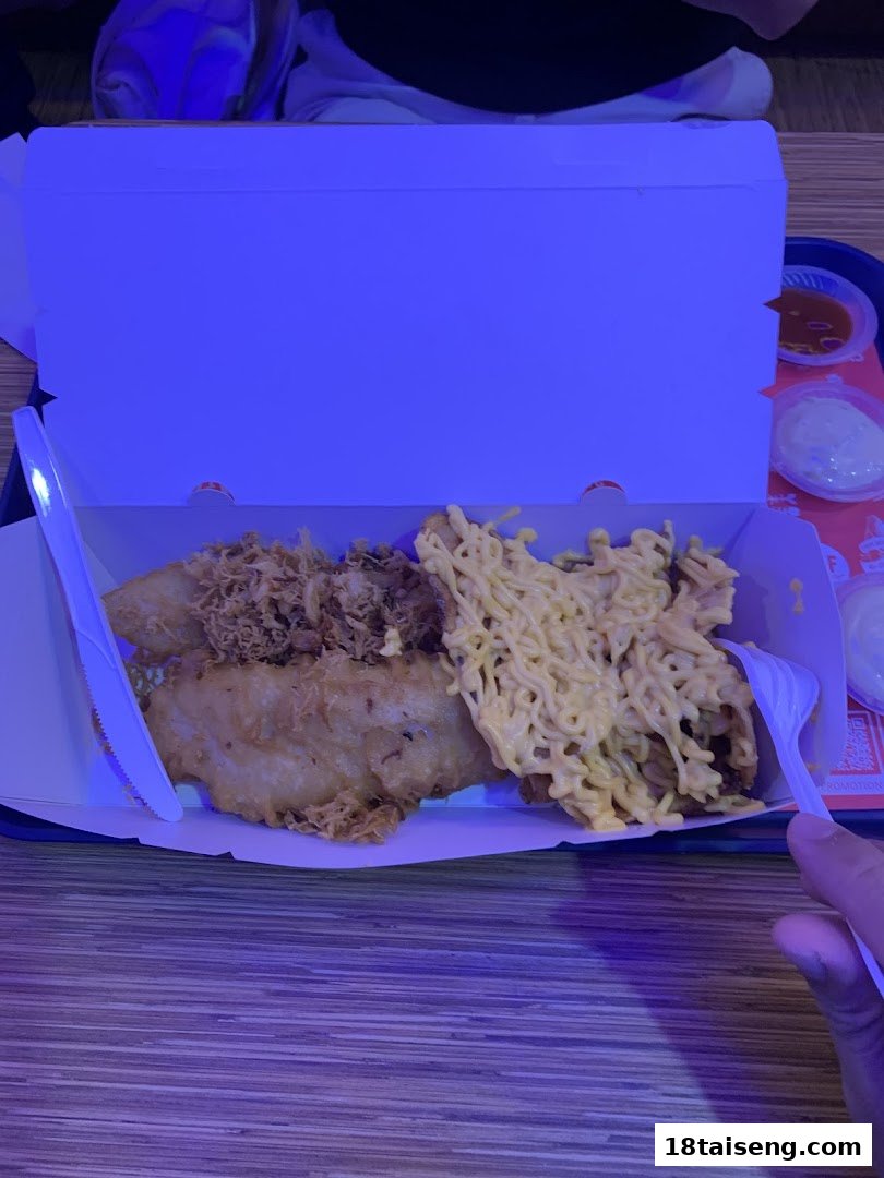A box of fried fish and chicken with noodles, sauces, and cutlery on a wooden table.