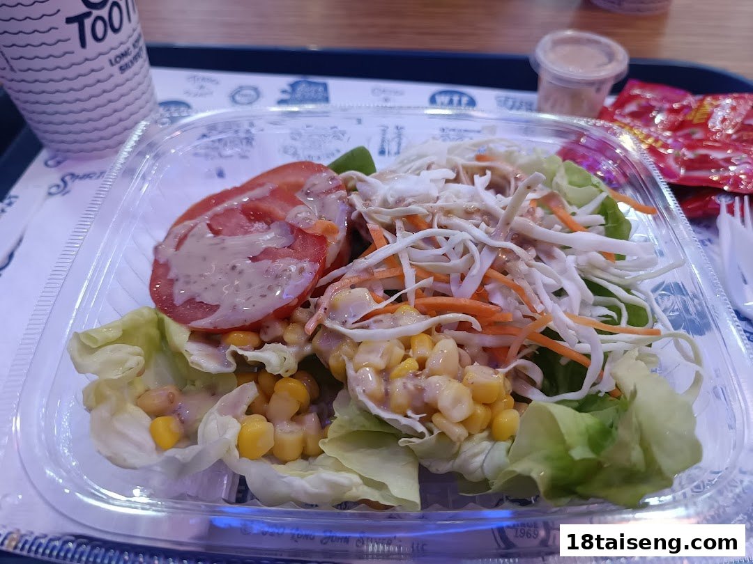 A fresh salad with corn, tomatoes, and dressing in a clear container on a tray.