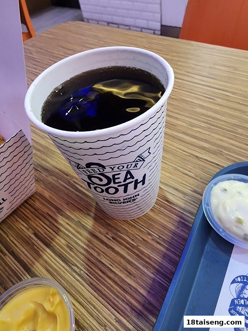 A Long John Silver's branded drink cup, sauces, and tray on a wooden table.