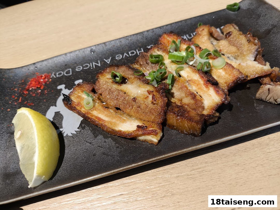 A plate of savory sliced pork belly garnished with green onions and a lemon wedge.