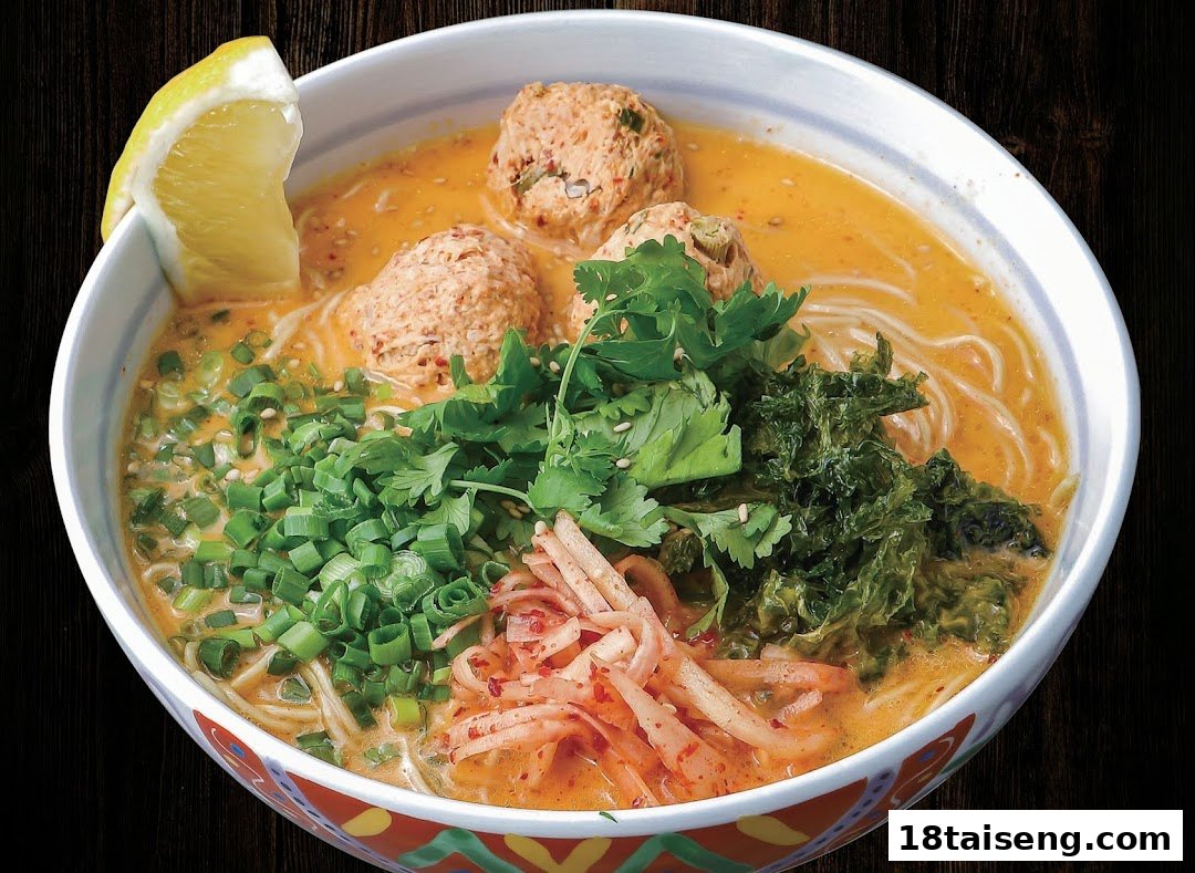 A vibrant bowl of ramen with chicken meatballs, fresh herbs, seaweed, and a lemon wedge.
