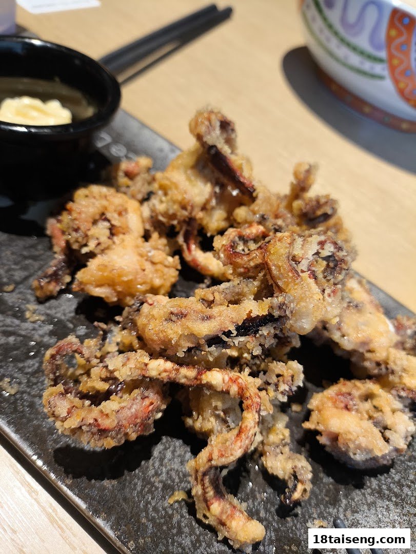 A close-up of crispy fried squid (calamari) served with a dipping sauce on a dark plate.
