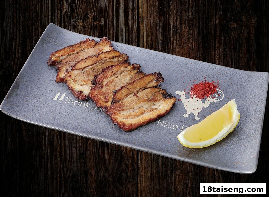 Slices of savory chashu pork belly with chili flakes and a lemon wedge on a grey plate.