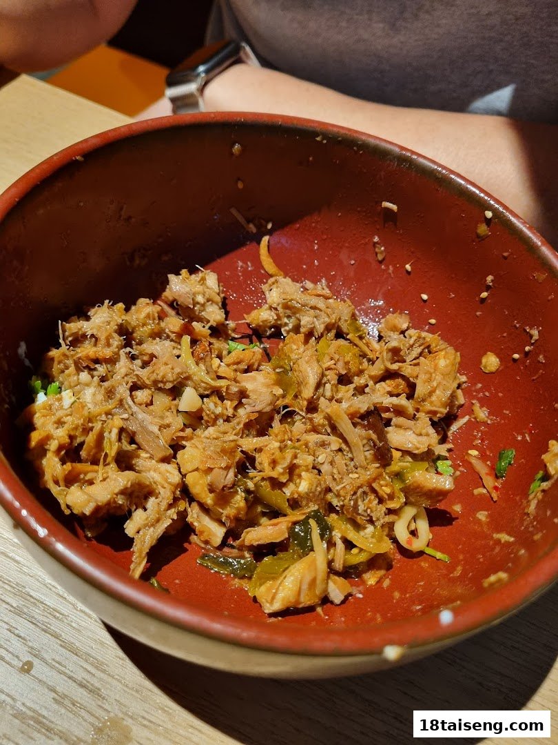 A close-up of a delicious shredded meat dish in a rustic red bowl at Marutama Ramen.