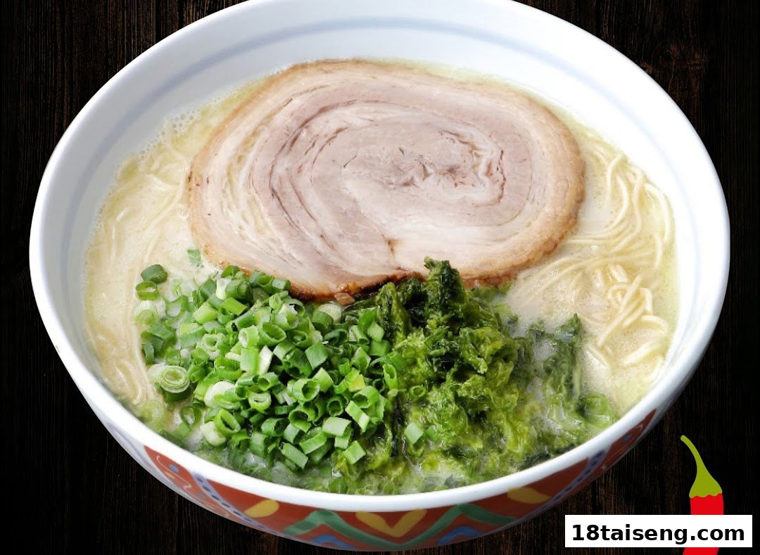 A close-up of a delicious bowl of ramen with chashu, green onions, and a vibrant green topping.