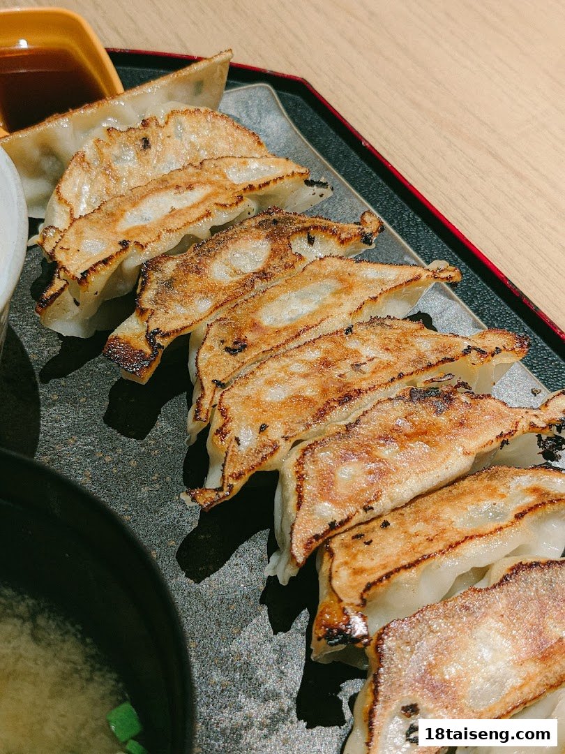 A close-up of perfectly pan-fried gyoza served with dipping sauce and a side of soup.