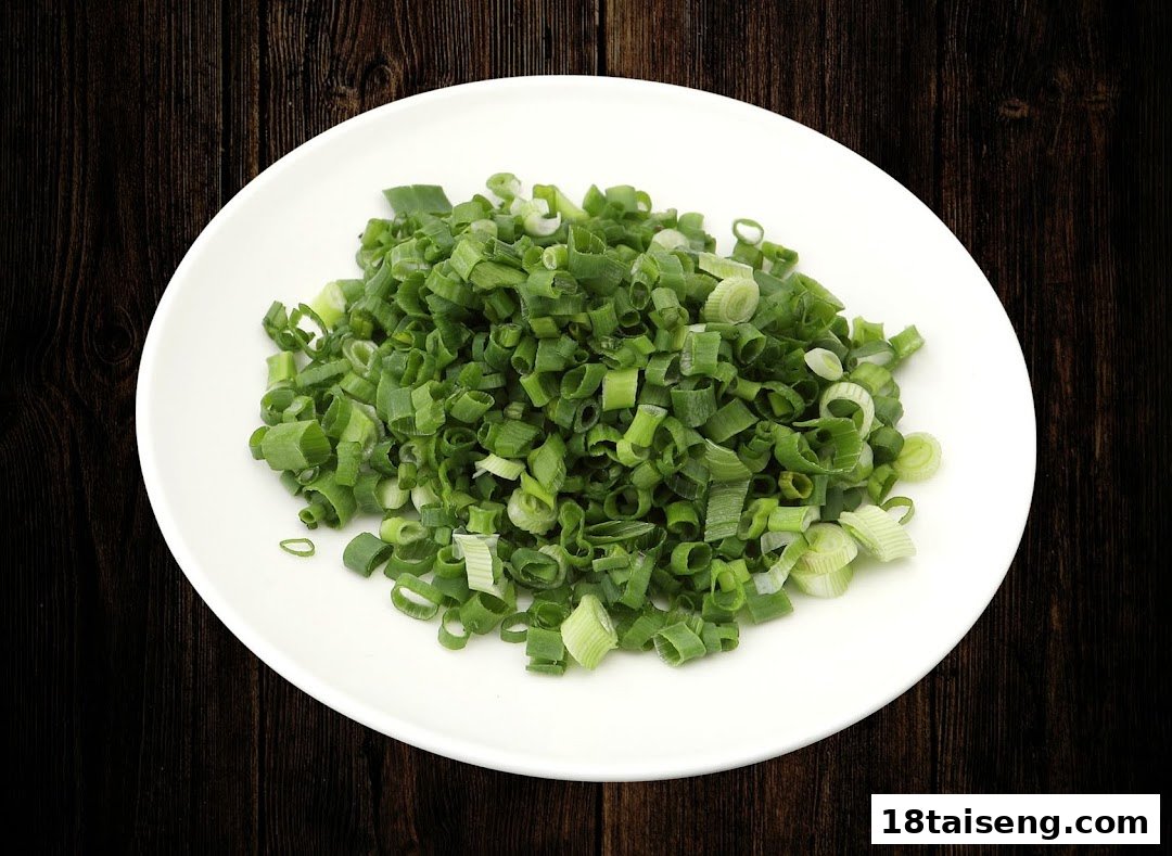 A white plate filled with freshly chopped green onions on a dark wooden surface.