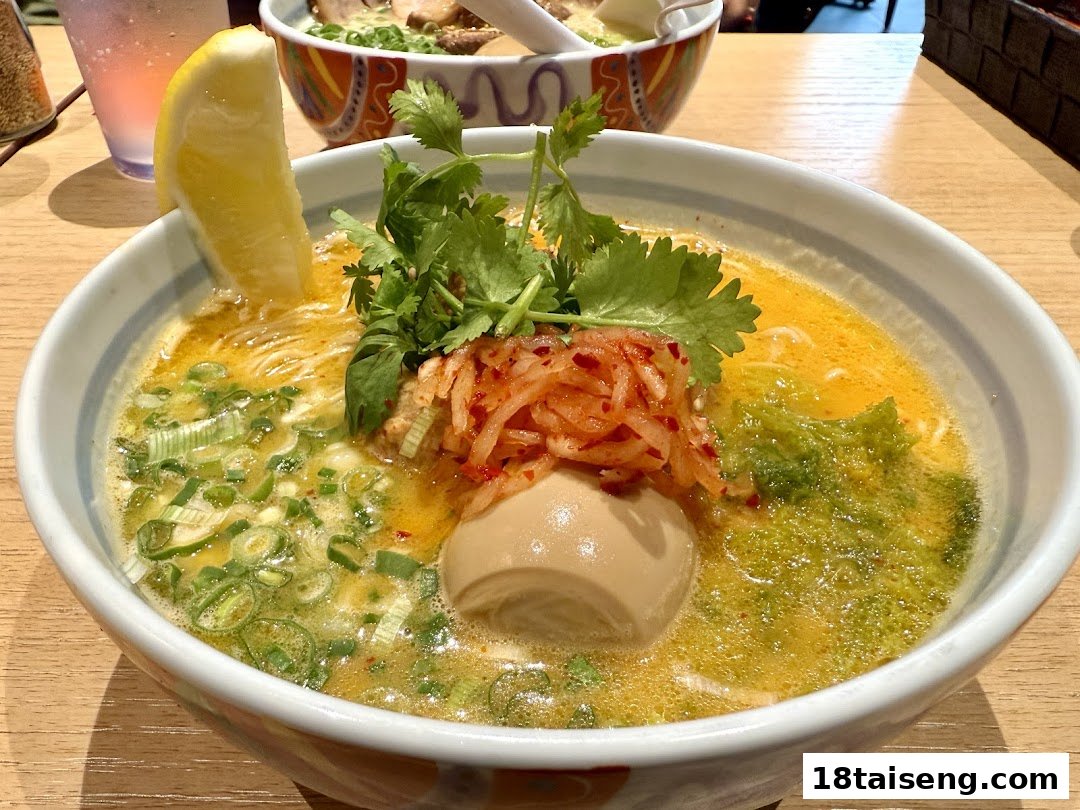 A vibrant bowl of ramen with various toppings, including a lemon wedge, egg, and greens.