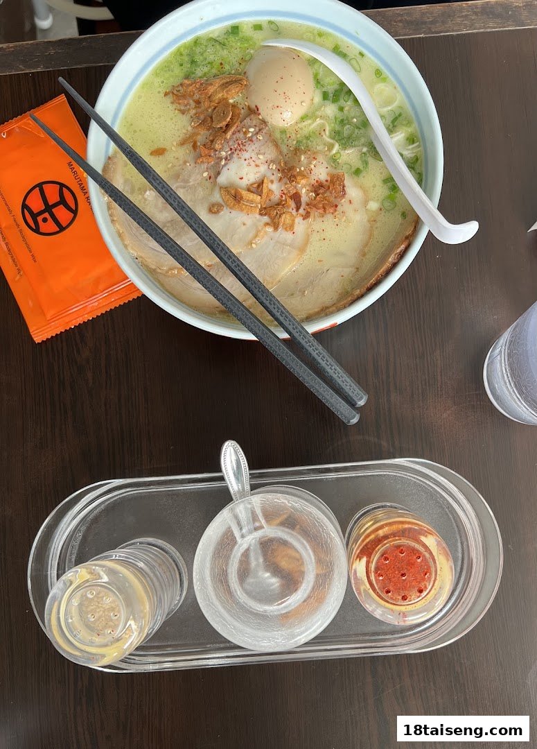 A delicious bowl of ramen with pork slices, egg, and condiments on a wooden table.