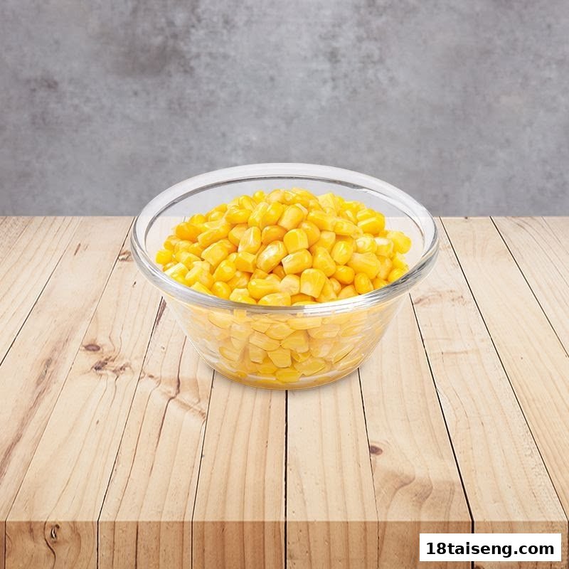 A clear glass bowl filled with bright yellow corn kernels sits on a light wooden table.