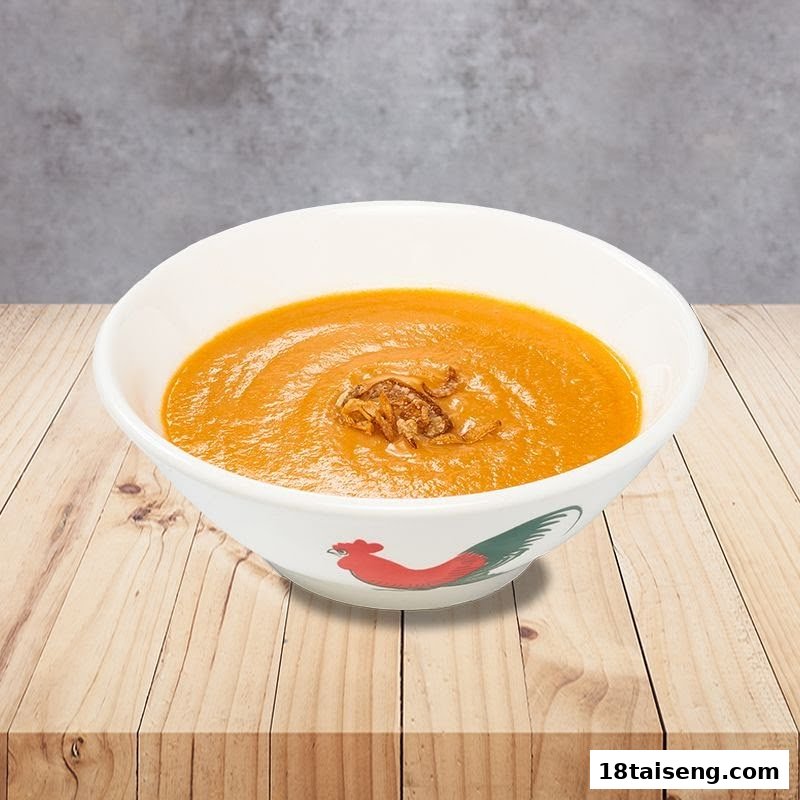 A bowl of creamy orange soup topped with crispy fried shallots on a wooden surface.