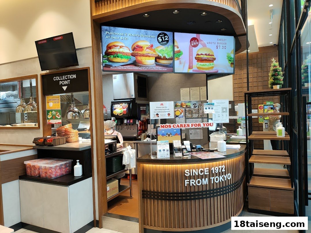 An interior view of MOS Burger, featuring the order counter, digital menu boards, and a collection point.