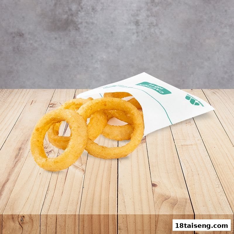 Golden onion rings spilling from a white paper bag onto a rustic wooden table.