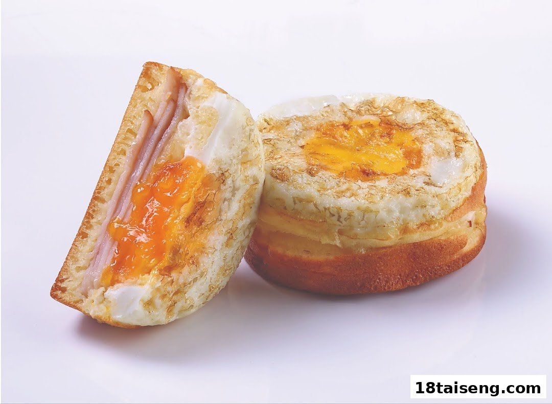 A savory bun or sandwich with ham and a fried egg, one piece cut open.