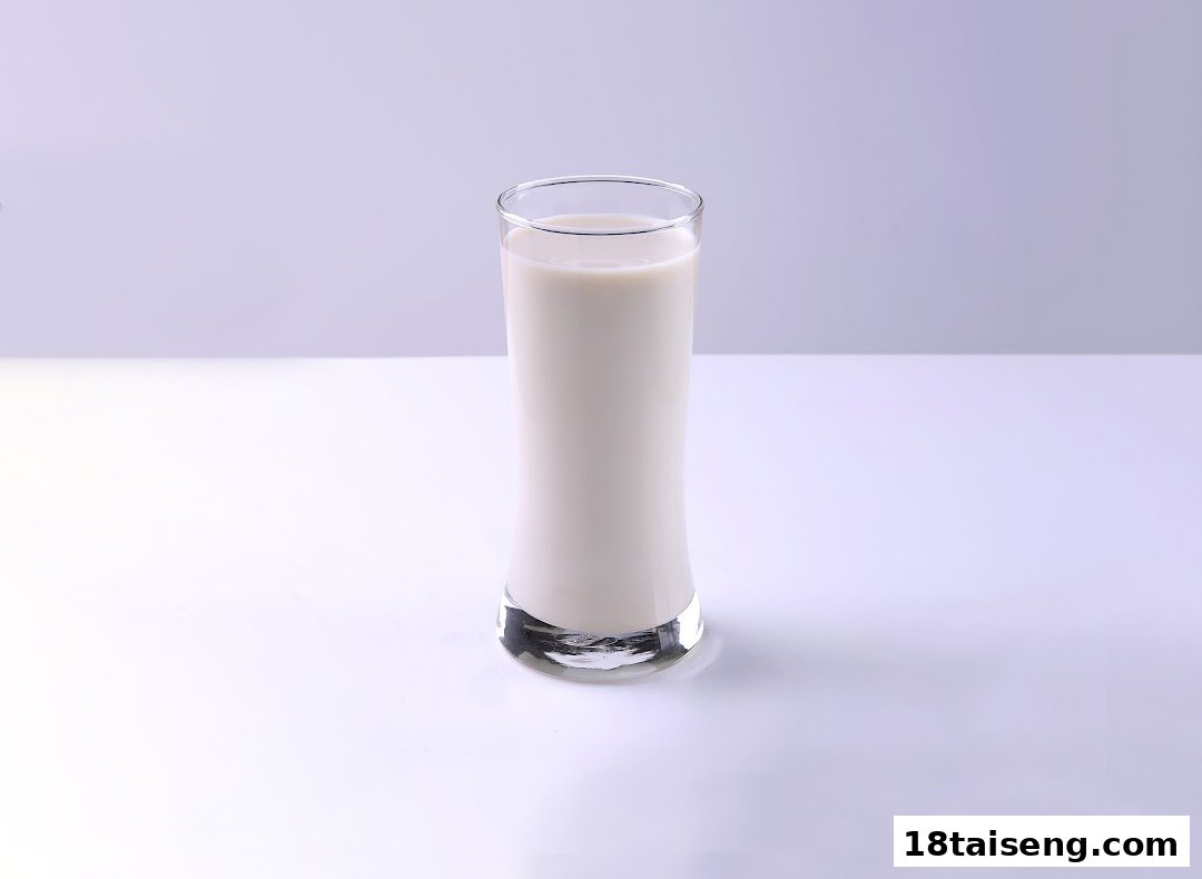 A tall glass filled with fresh, creamy soy milk on a clean white surface.