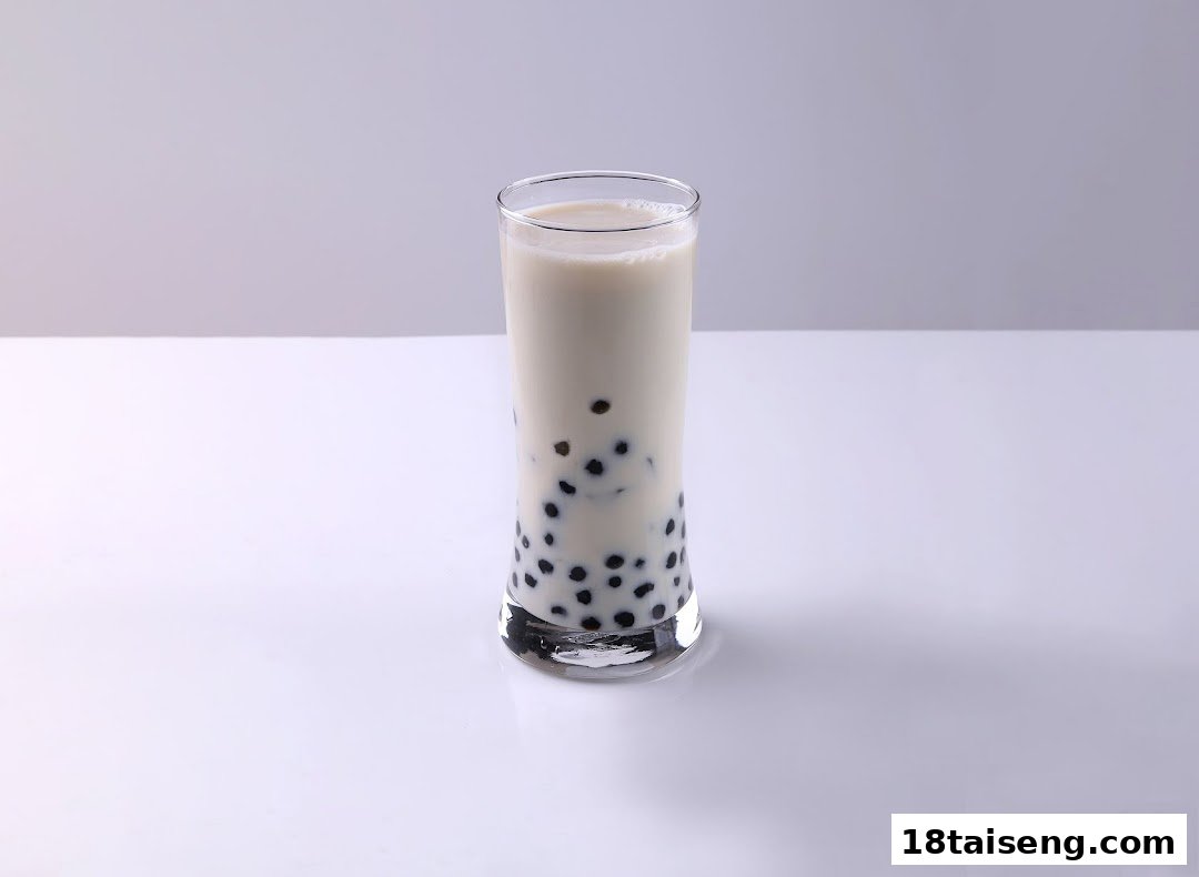 A tall glass of milky bubble tea with dark tapioca pearls on a white surface.