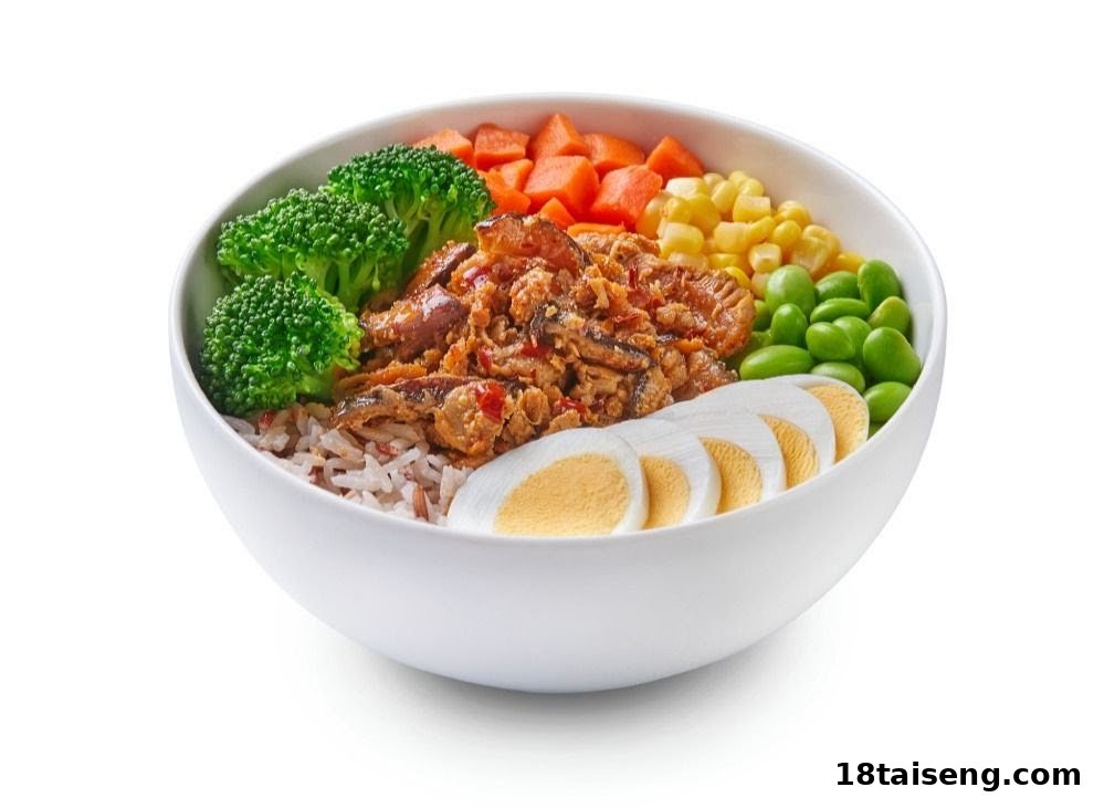 A vibrant food bowl featuring rice, protein, broccoli, carrots, corn, edamame, and sliced eggs.
