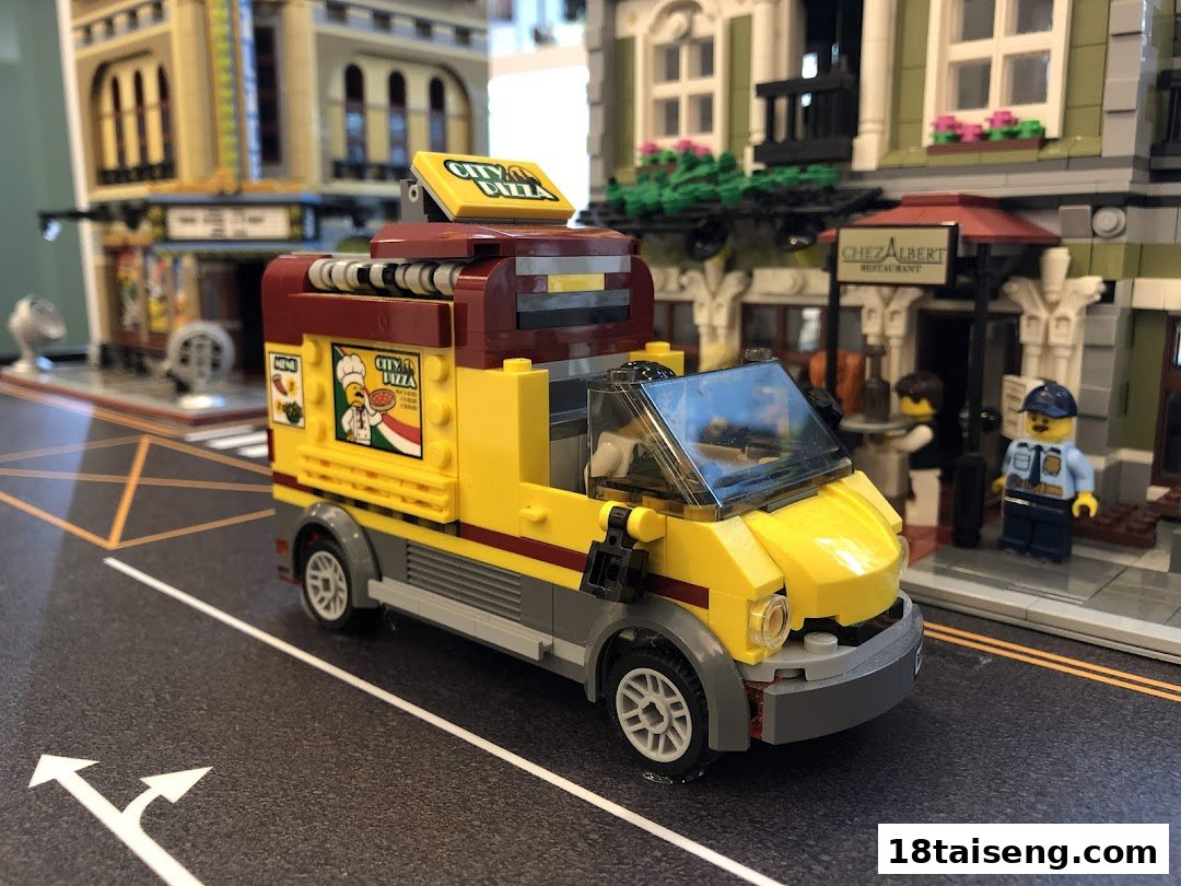 A detailed LEGO City pizza delivery truck model displayed on a miniature street scene with buildings.