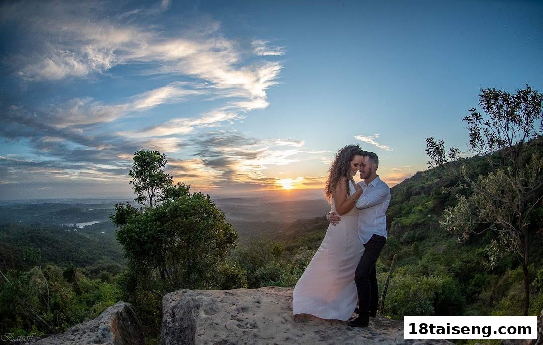 A couple embraces on a mountaintop overlooking a scenic valley at sunset, showcasing beautiful photography.