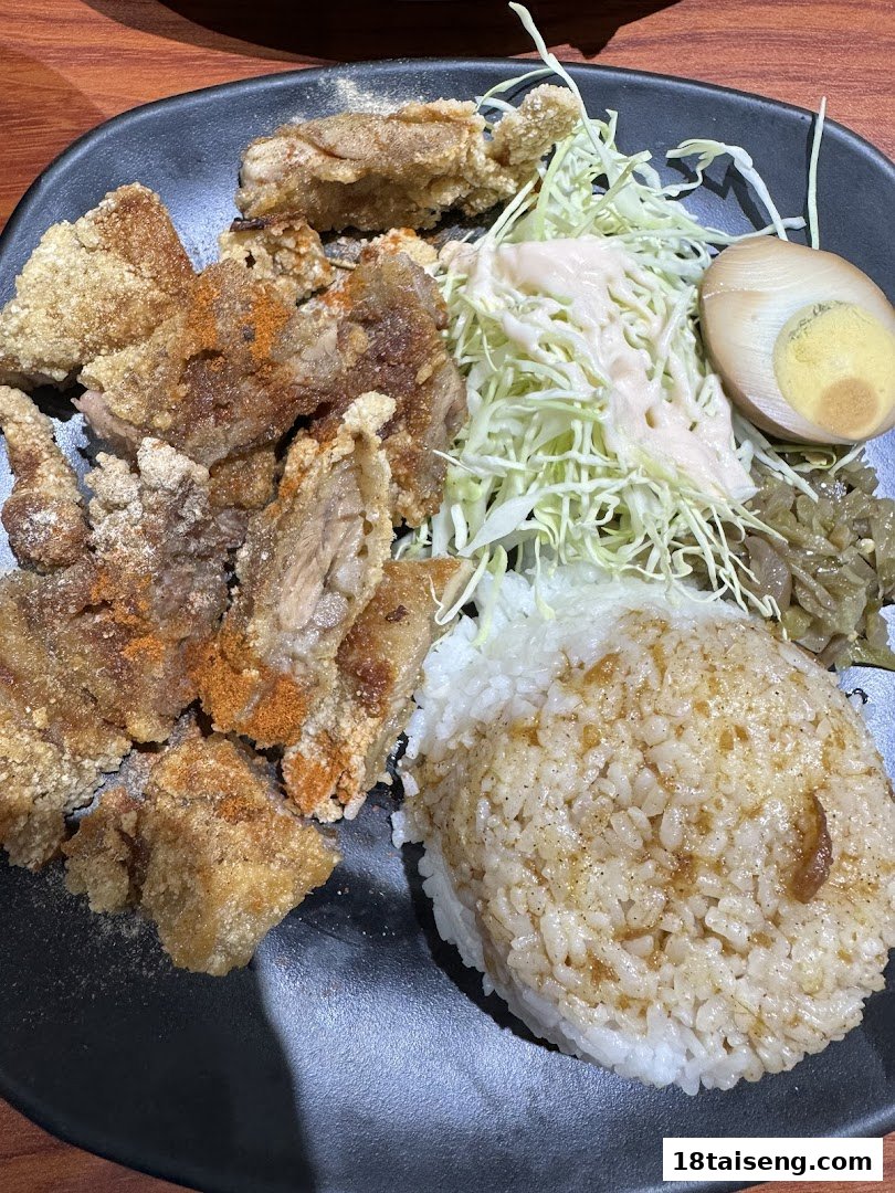 A plate of crispy Taiwanese fried chicken with seasoned rice, shredded cabbage, and a tea egg.