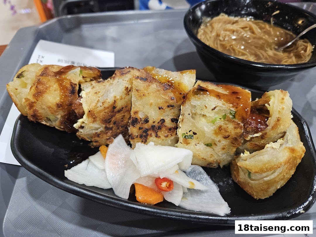 A plate of Taiwanese savory pancake roll with pickled vegetables and a bowl of vermicelli noodles.