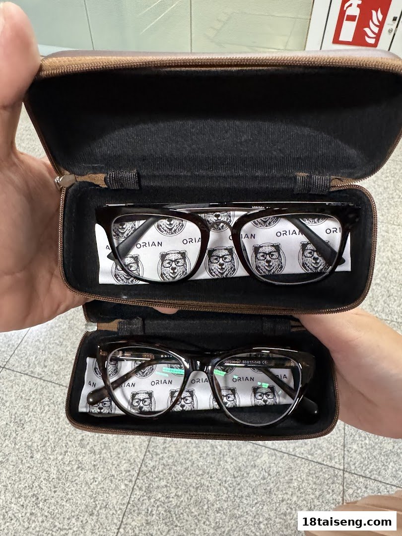 Two pairs of stylish eyeglasses in their cases, featuring Orian branded cleaning cloths.
