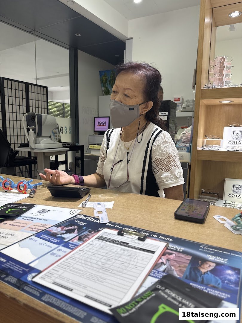 A customer consults at an optical shop counter with eye care equipment and product displays.