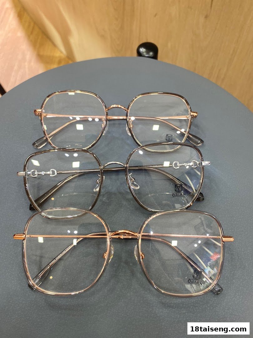 A close-up of several stylish eyeglasses with metallic frames on a grey surface.