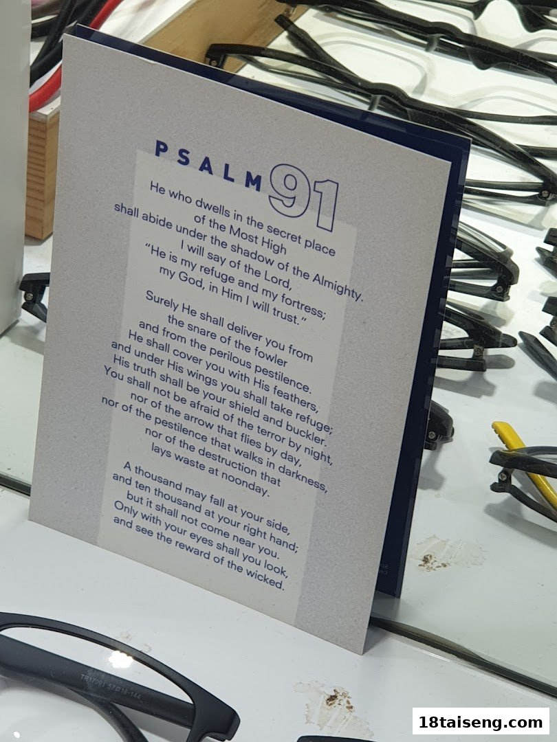 A card displaying Psalm 91 text, surrounded by eyeglasses, likely in an optical shop.
