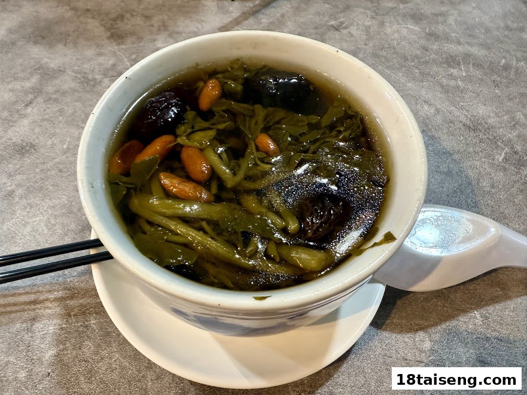 A close-up of a bowl of healthy vegetarian soup with greens, goji berries, and dates.