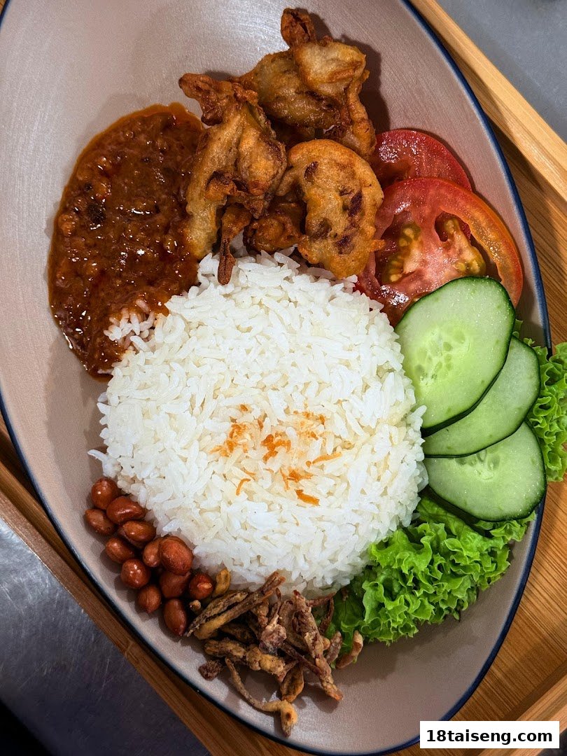 A vibrant plate of vegetarian Nasi Lemak with rice, sambal, fried mock meat, peanuts, and fresh vegetables.