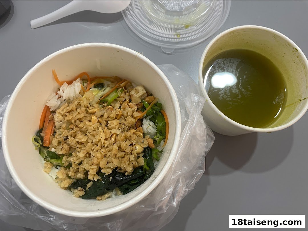 A vegetarian meal bowl with rice, vegetables, and peanuts, alongside a green drink.