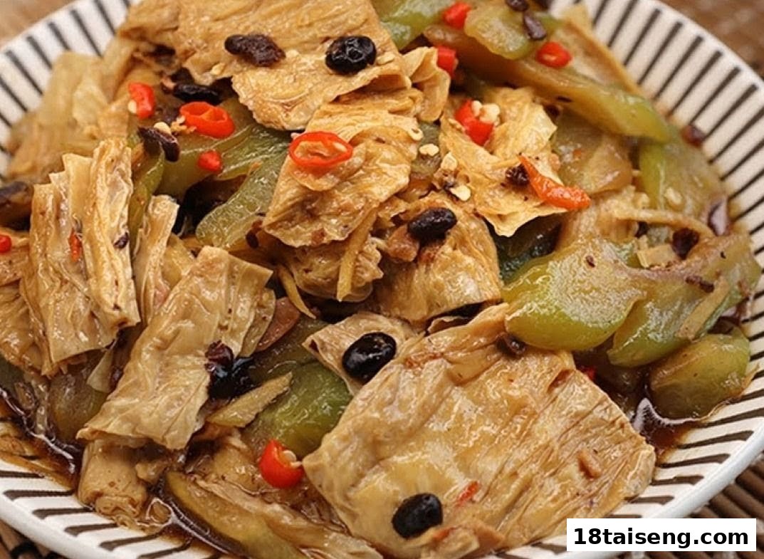 A close-up of a savory vegetarian dish featuring tofu skin, bitter melon, and chili in a dark sauce.