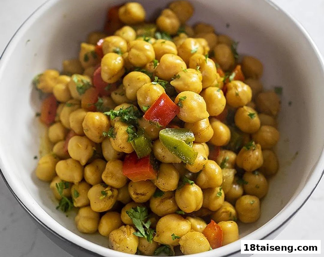 A close-up of a bowl filled with seasoned chickpeas, diced red and green bell peppers, and fresh herbs.
